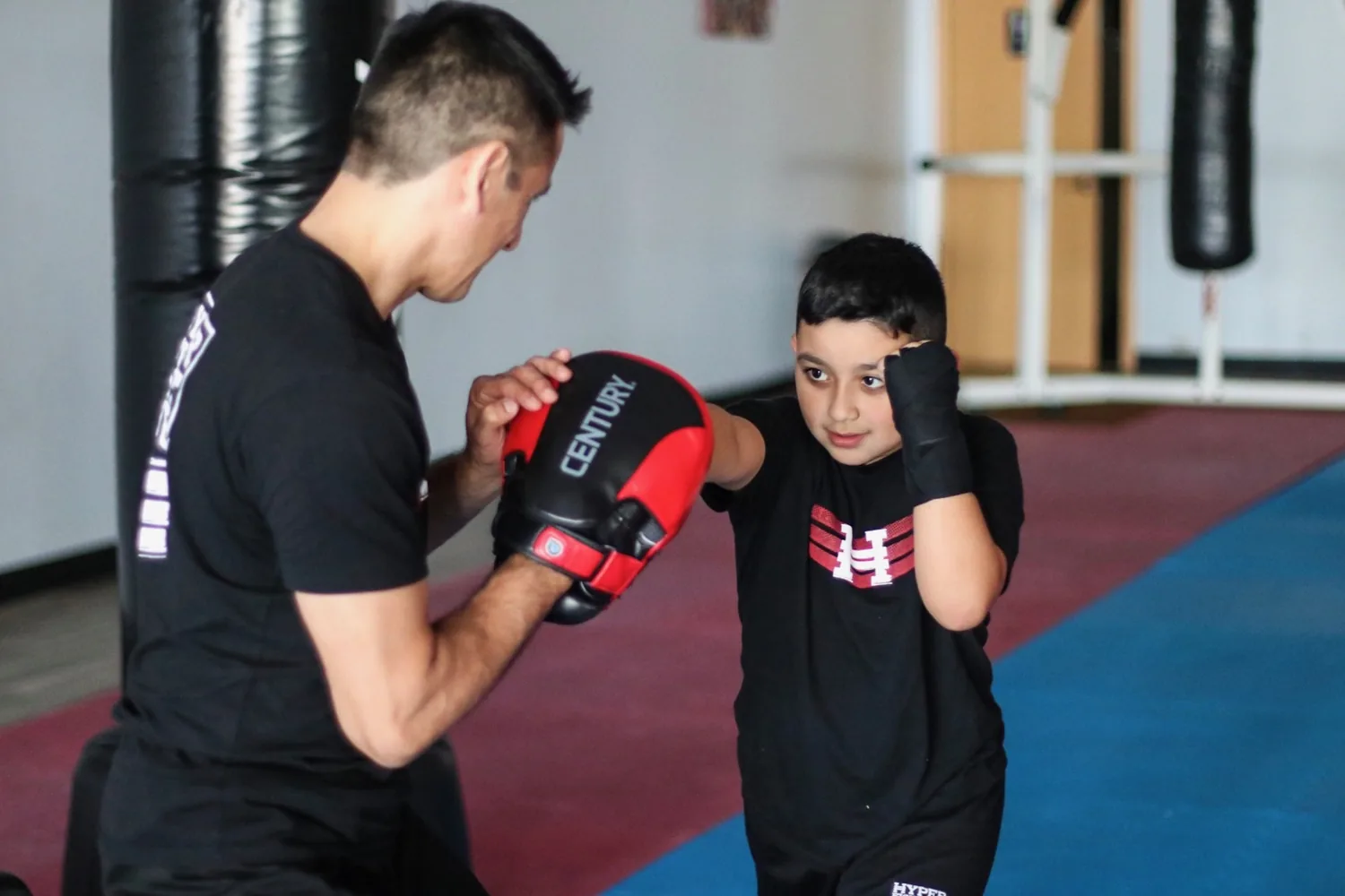 A young Legacy student practicing punches with an instructor holding focus mitts
